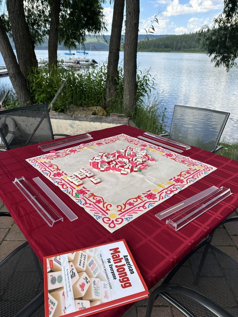 Mahjong game set up on a table outdoors by a lake, with tiles and racks ready.